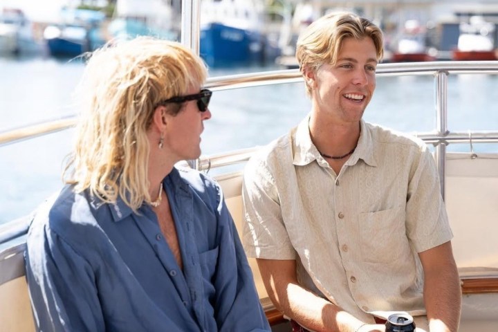 Two people chatting and smiling on a boat with water and buildings in the background.